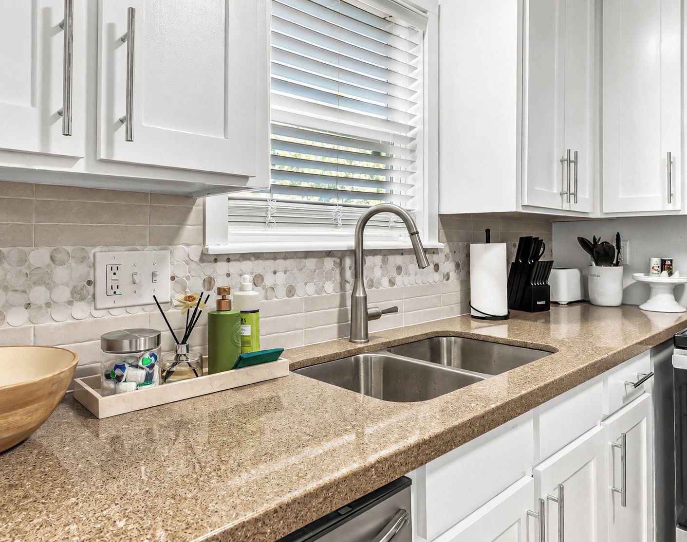A kitchen with white cabinets, a granite countertop, a double sink, and a window with blinds.