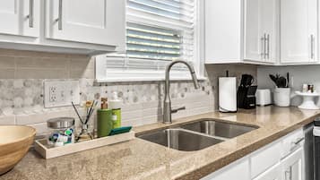 A kitchen with white cabinets, a granite countertop, a double sink, and a window with blinds.