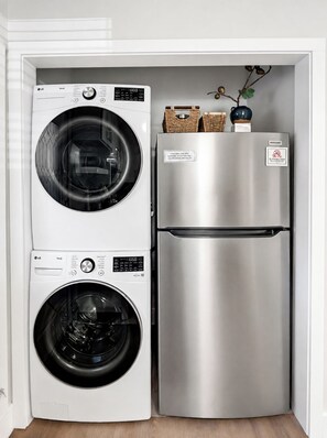 Une cuisine compacte équipée d’un réfrigérateur en acier inoxydable et de deux machines à laver blanches.