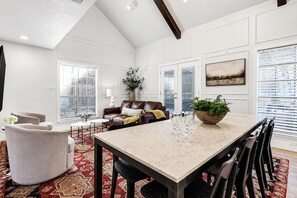 A spacious living area with a high ceiling, a dining table with chairs, a sofa, and a coffee table. - Northgate: Closest Home to Aggieland! 3BR, 2.5BA (College Station)
