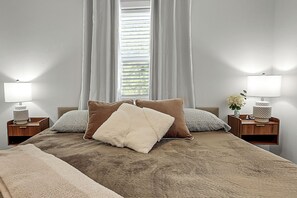 Une chambre à coucher comprenant un lit, deux tables de chevet, une fenêtre avec des rideaux et deux lampes de chevet.