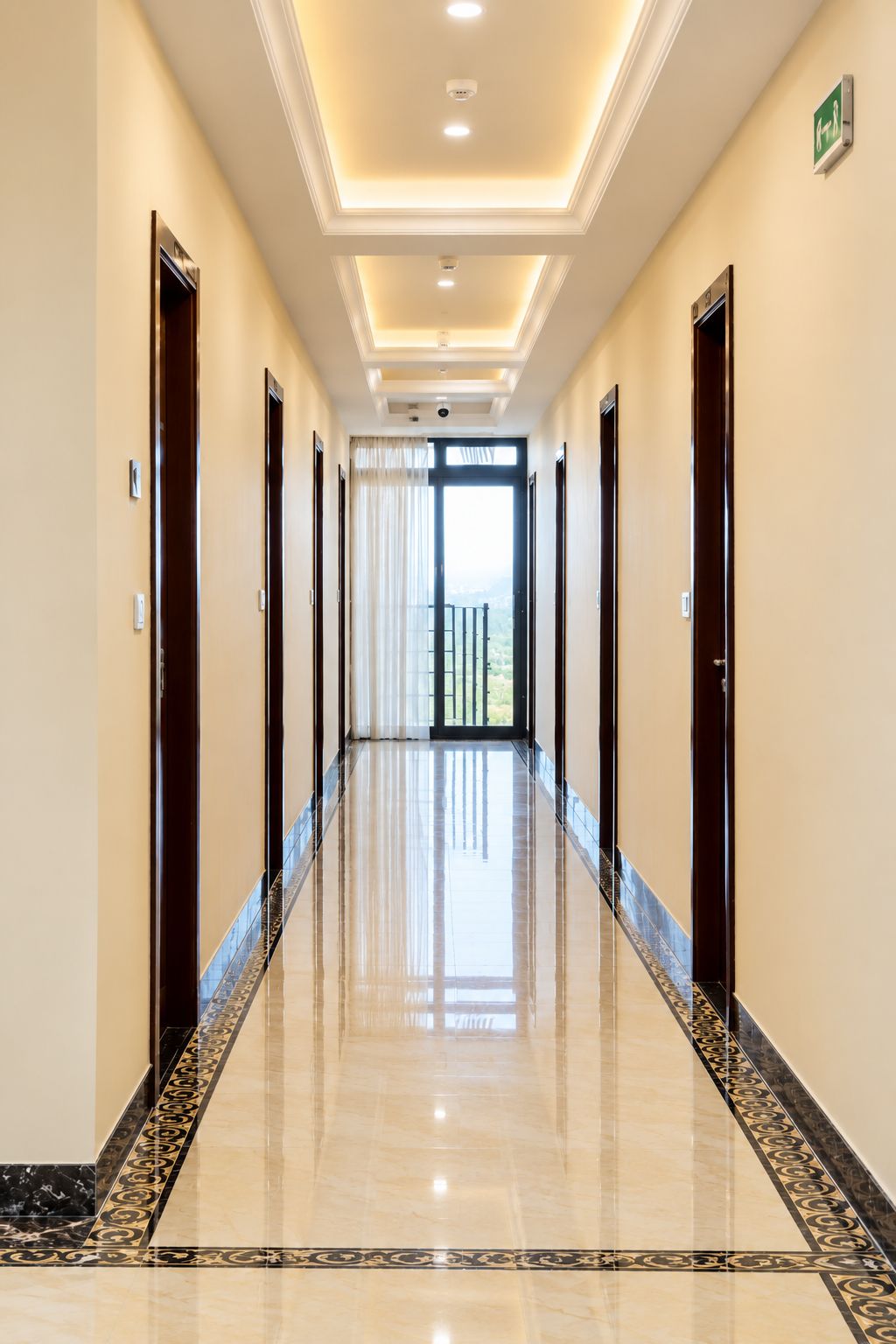 A hotel hallway with a polished floor, doors on both sides, and a view of the outdoors through a large window.