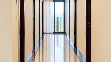 A hotel hallway with a polished floor, doors on both sides, and a view of the outdoors through a large window.