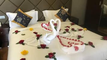 Cama com colcha branca, almofadas decorativas e arranjo de toalhas em formato de coração.