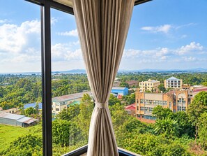 Vista desde una ventana con cortinas, con vistas a un paisaje urbano con edificios y zonas verdes.