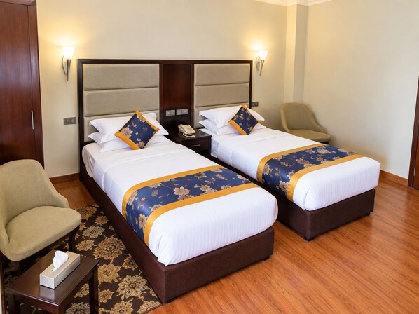 A hotel room with two beds, a desk, a chair, and a bedside table.