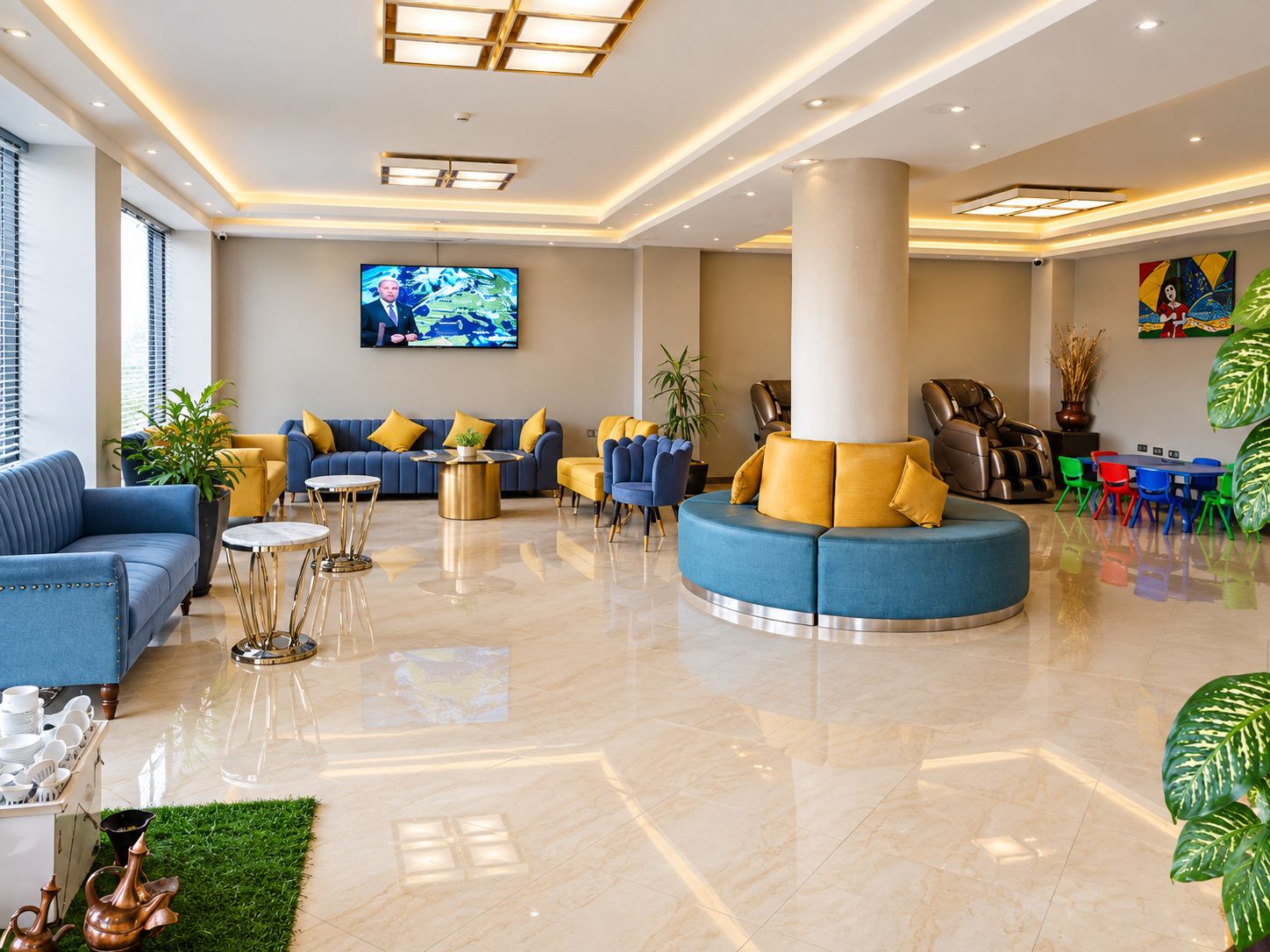 A spacious lobby with a large seating area, a television mounted on the wall, and a variety of plants.