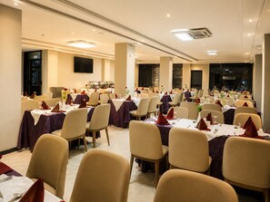 Un salón de banquetes con varias mesas dispuestas para comer, sillas alrededor de cada una y una zona de bufé al fondo.