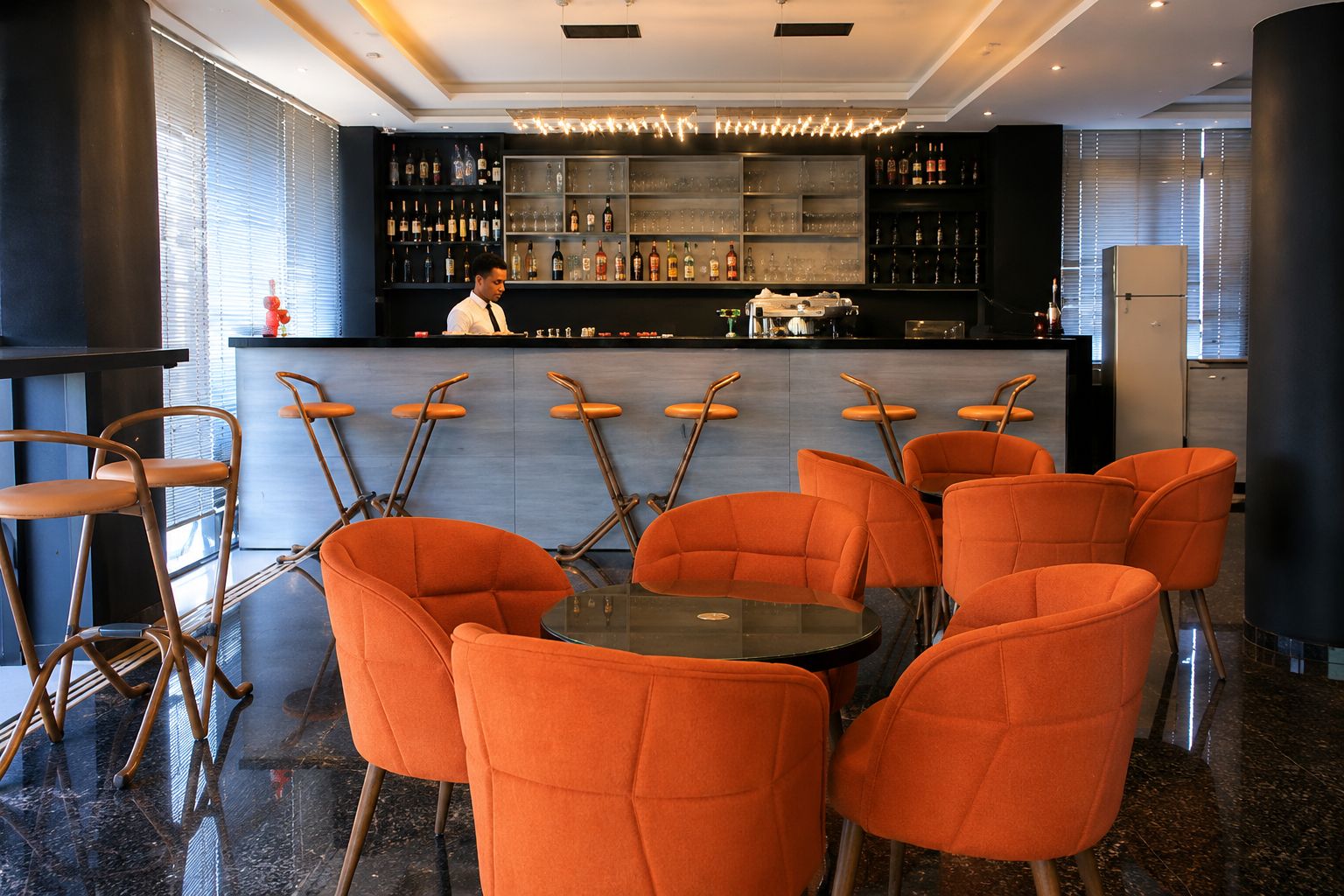 A bar area with a bartender, orange chairs, and a bar counter with various bottles.