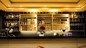 A bar area with shelves of bottles and glasses, a potted plant, and a bar counter.