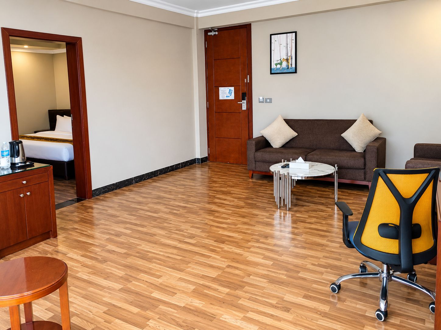 Quarto de hotel com piso de madeira, um sofá, uma mesa de centro, uma escrivaninha e uma cadeira.