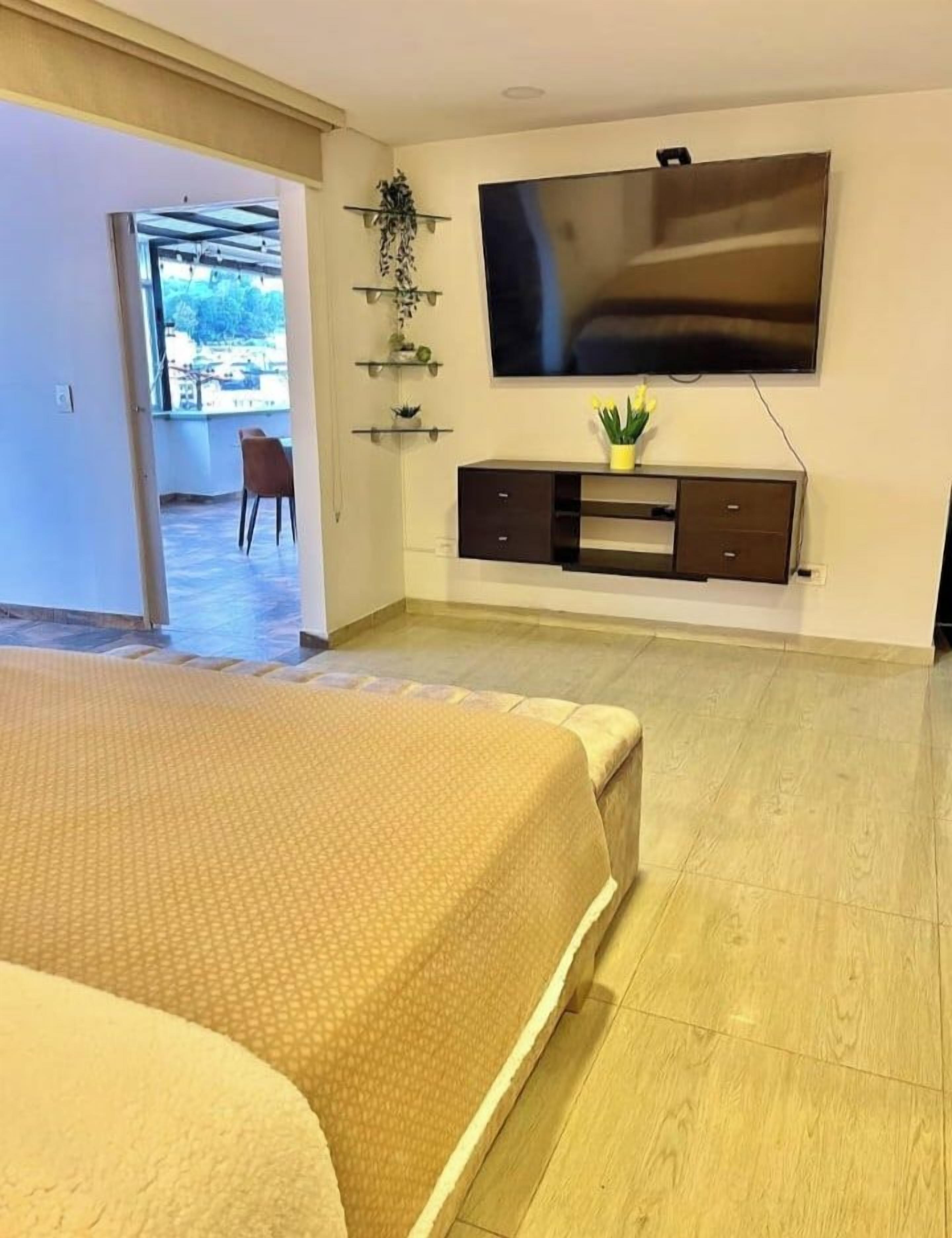 Ein Schlafzimmer mit einem Bett, einem an der Wand montierten Fernseher, einer kleinen Kommode und einem Fenster.