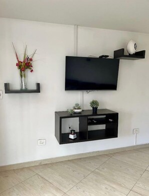 A modern living room with a flat-screen TV mounted on the wall, a black entertainment unit below, and a small shelf with decorative items. - Sumptuous and Spacious - Class 5 Residential Area (Estrato 5) (Manizales)