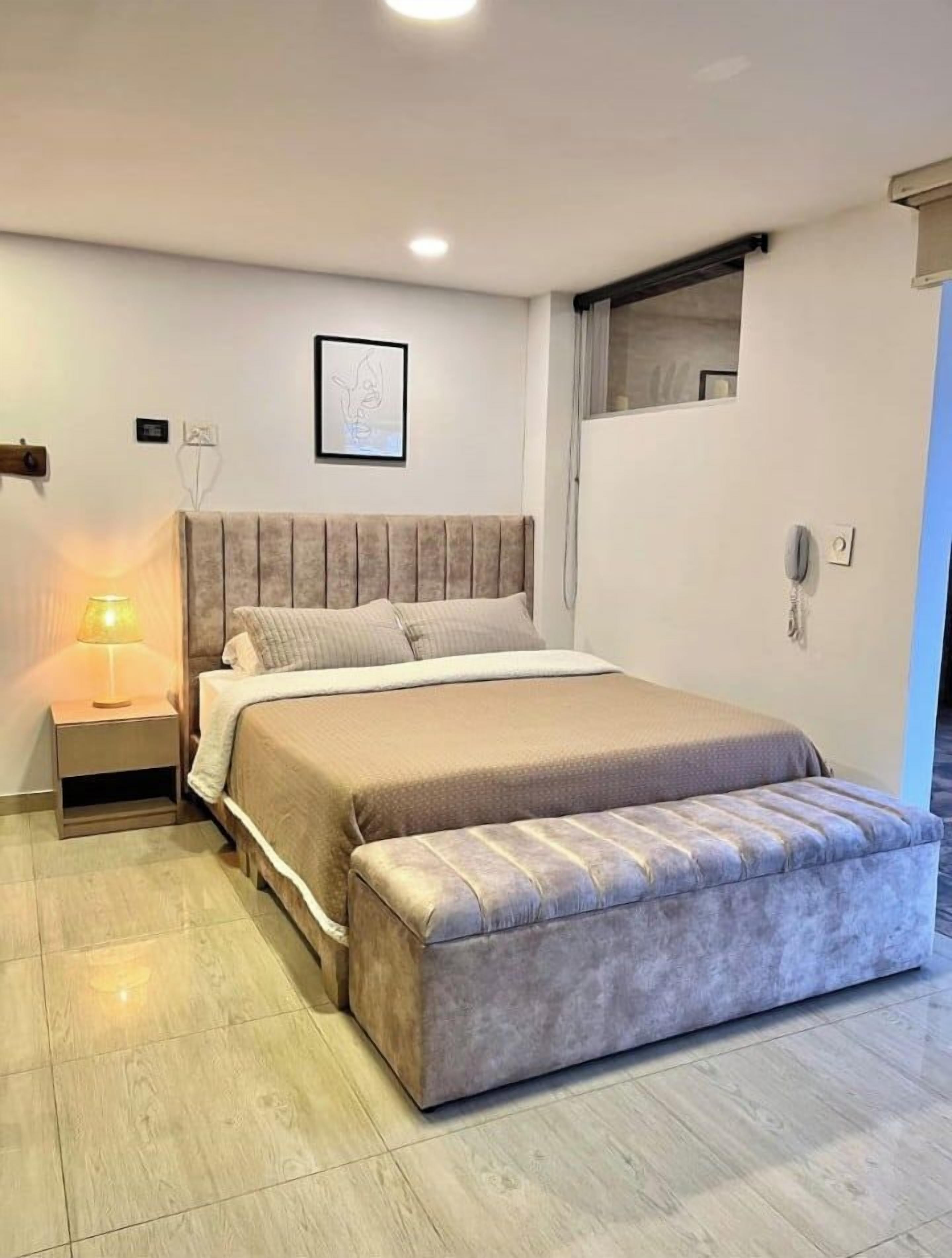 Un dormitorio moderno con cama, mesita de noche y una ventana pequeña.
