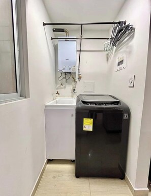A compact kitchen with a white washing machine, a black refrigerator, and a water heater on the wall. - Sumptuous and Spacious - Class 5 Residential Area (Estrato 5) (Manizales)