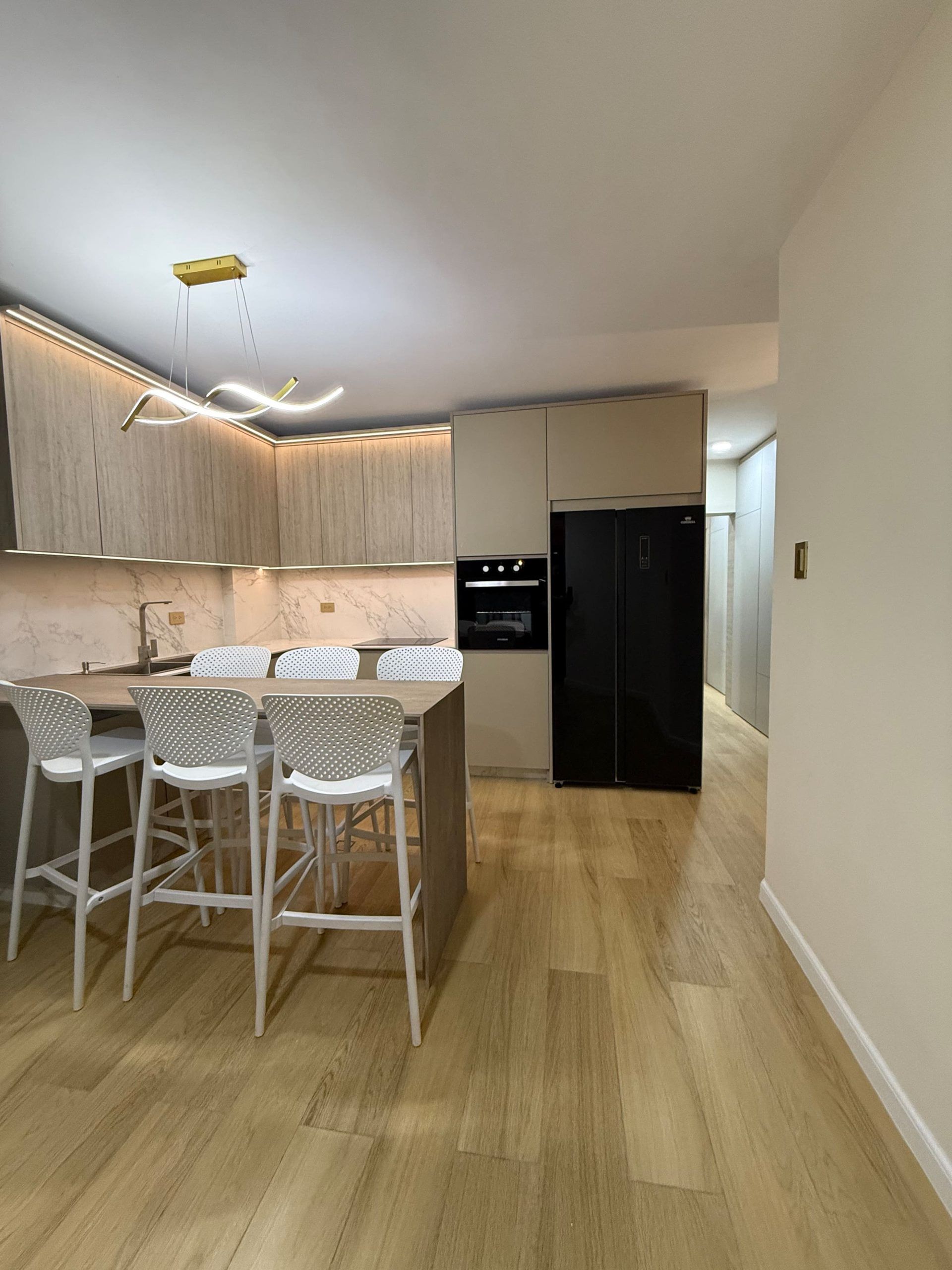 A modern kitchen with a bar area, wooden cabinets, and a black refrigerator.