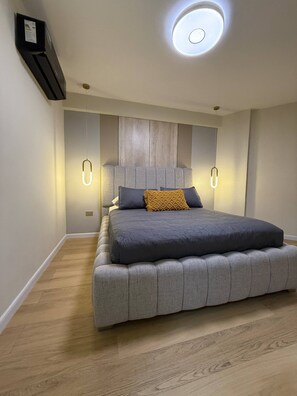 A modern bedroom with a large bed, a headboard with built-in lighting, and a ceiling light fixture.