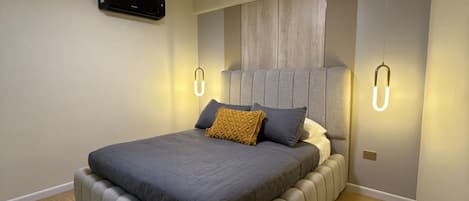 A modern bedroom with a large bed, built-in headboard, and wall-mounted lighting.