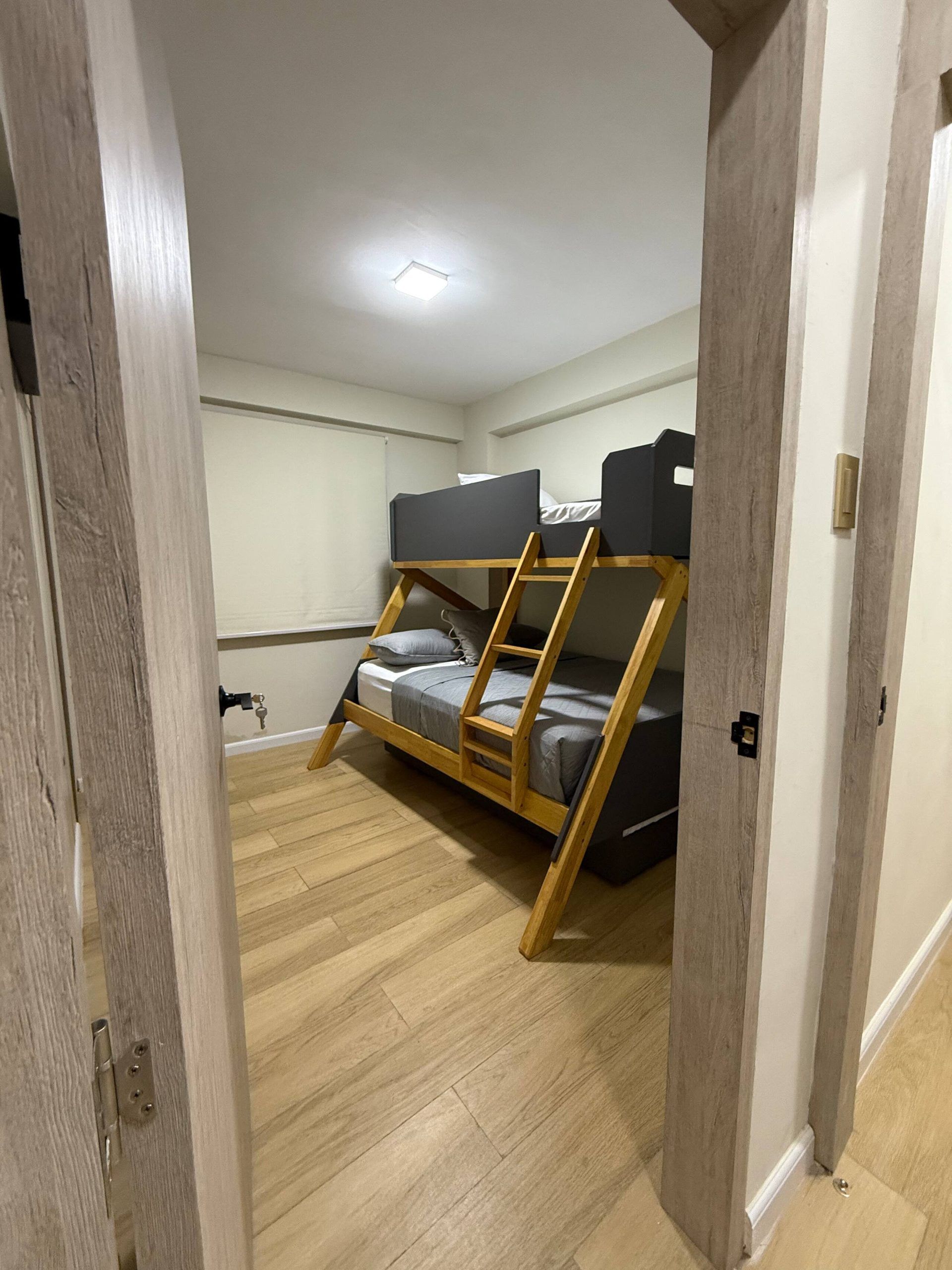 Une chambre avec un lit superposé, un plancher en bois et un luminaire au plafond.