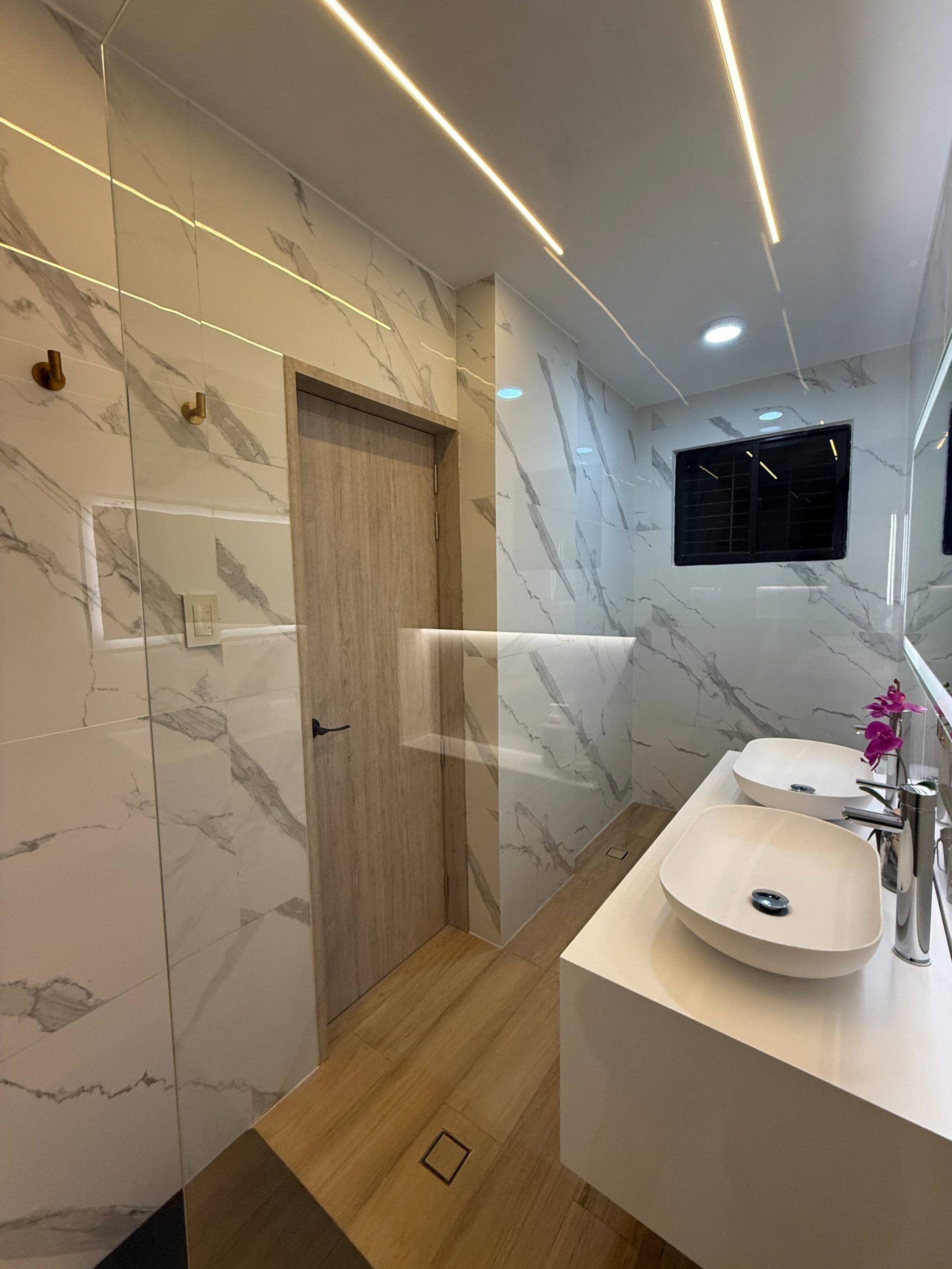 Un bagno moderno con pareti in marmo, una porta in legno e due lavabi con rubinetti.