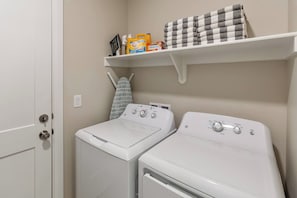 A laundry area with two white washing machines, a drying rack, and a shelf with folded towels and cleaning products. - Close to National and State Parks - Heated Pool, Hot Tub, Bunk Beds (Washington)