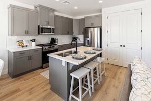 A modern kitchen with grey cabinets, a stainless steel refrigerator, a microwave, and a stove. There is a small island with stools and a sink. - Close to National and State Parks - Heated Pool, Hot Tub, Bunk Beds (Washington)