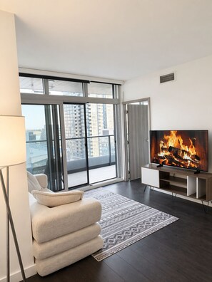 Een moderne woonkamer met een grote televisie waarop een haard, een bank en een uitzicht op hoge gebouwen door grote ramen te zien is.