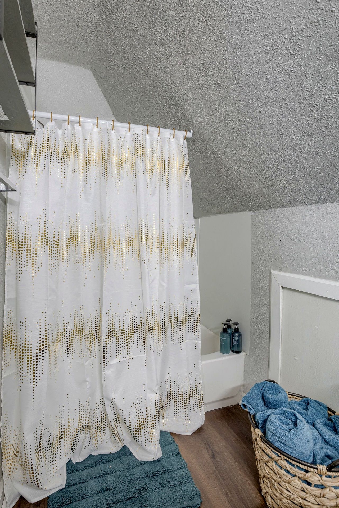 A bathroom with a shower curtain, a bathtub, a blue towel, and a wicker basket.