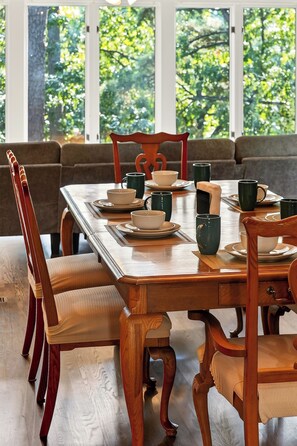 A dining table set with plates, bowls, and cups, surrounded by wooden chairs with cushioned seats. - Wooded Whitetail Retreat at Beaver Lake - Sleeps 14 - Games, Decks & Lake Access (Rogers)