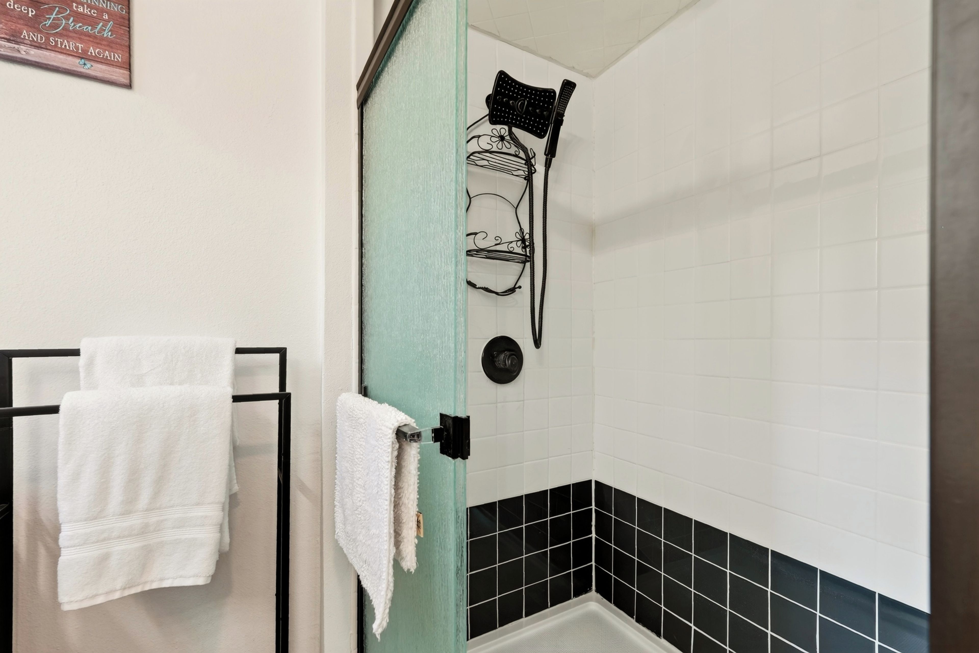 A bathroom with a shower, a towel rack with two towels, and a decorative sign on the wall.