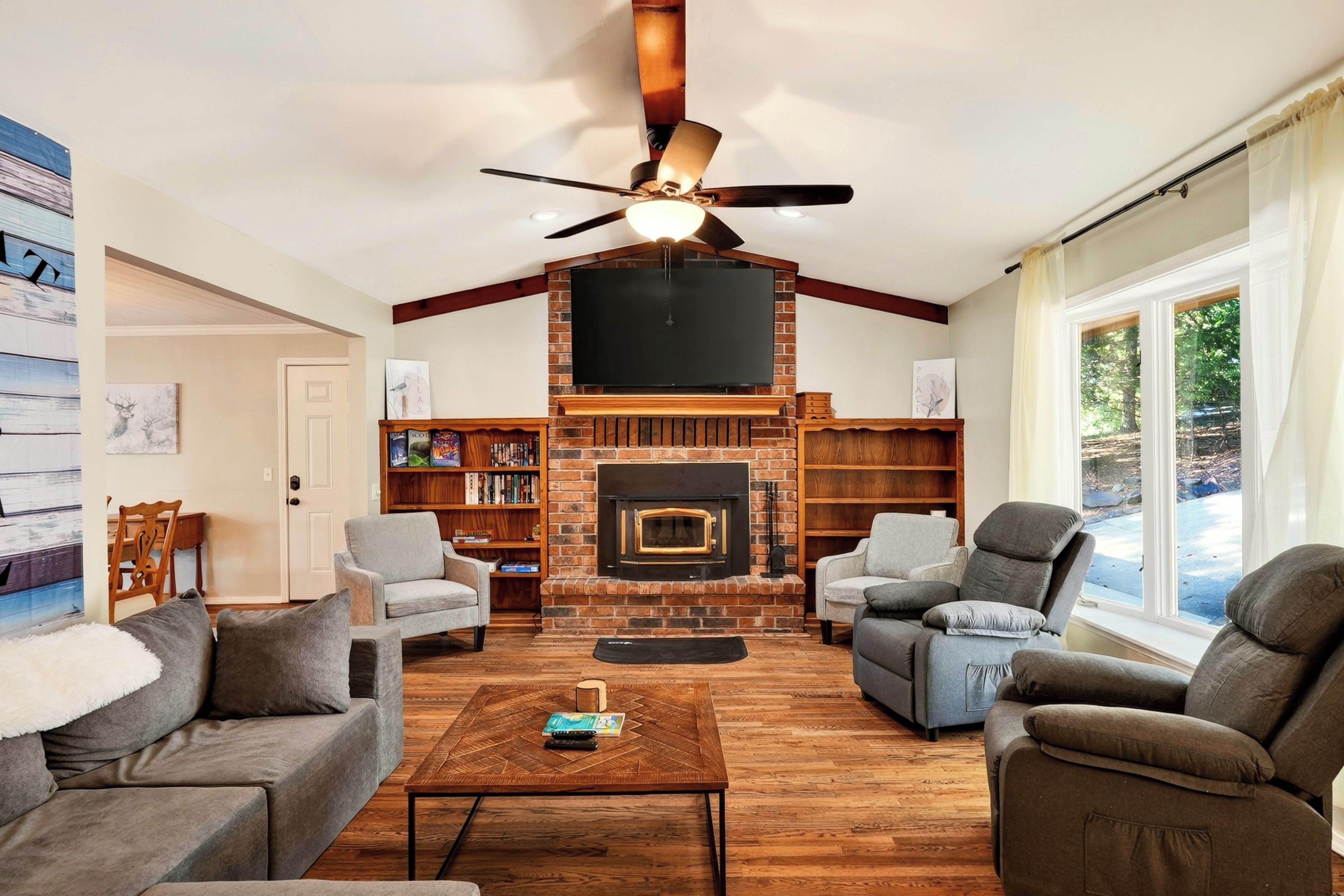 A living room with a fireplace, ceiling fan, and large windows.