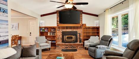 Una sala de estar con chimenea, ventilador de techo y ventanas amplias.