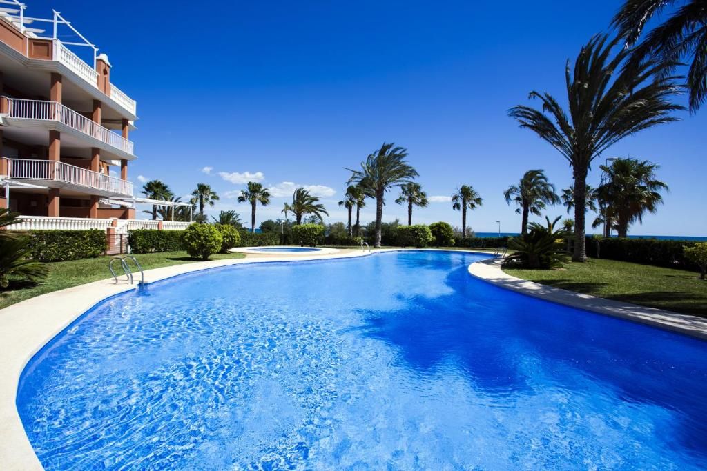 A swimming pool with a clear blue water surface, surrounded by palm trees and a building with balconies.