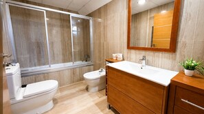Une salle de bain moderne équipée d’une douche, de toilettes, d’un bidet et d’un meuble-lavabo avec un miroir.
