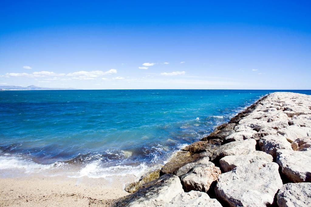 A rocky shoreline with clear blue water and a distant mountain range.
