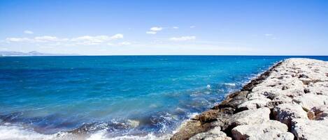 A rocky shoreline with clear blue water and a distant mountain range.