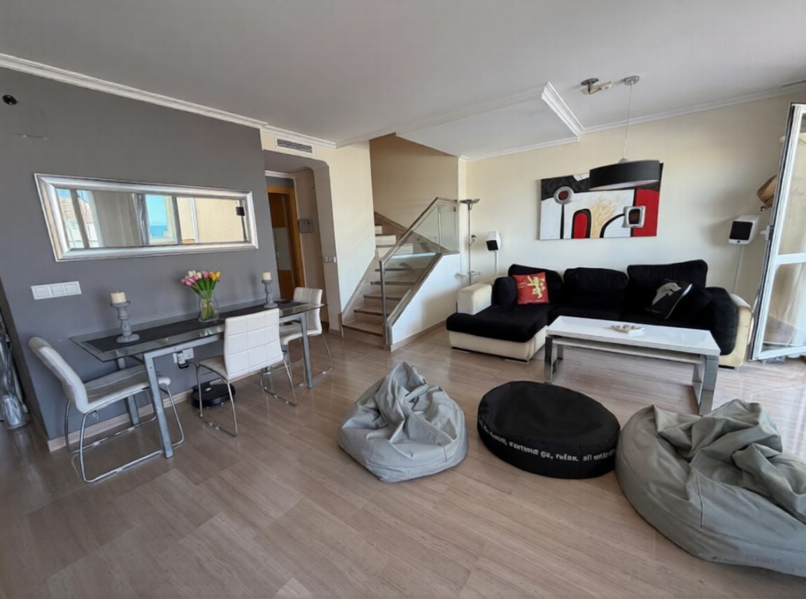 A modern living room with a dining area, a staircase, and a large window.