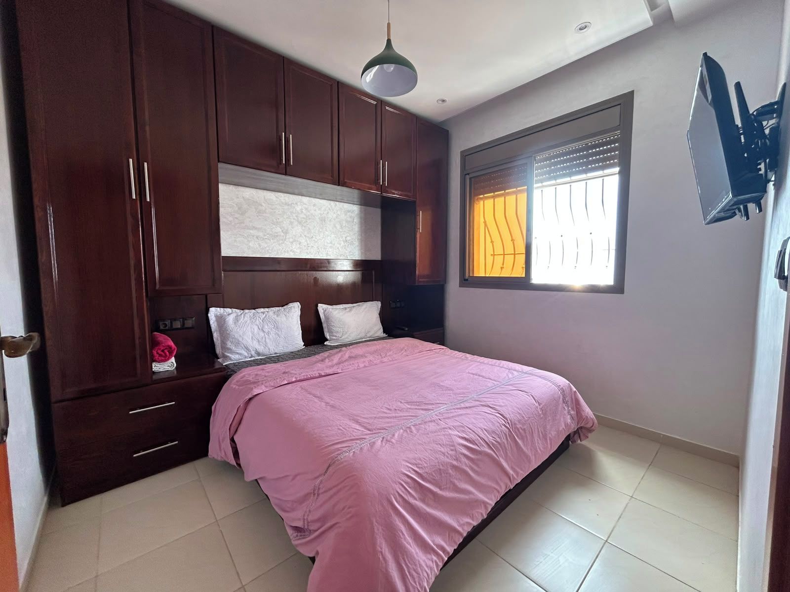 Un dormitorio con una cama, armario de madera y ventana con persianas.