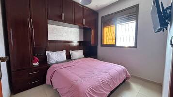 Un dormitorio con una cama, armario de madera y ventana con persianas.