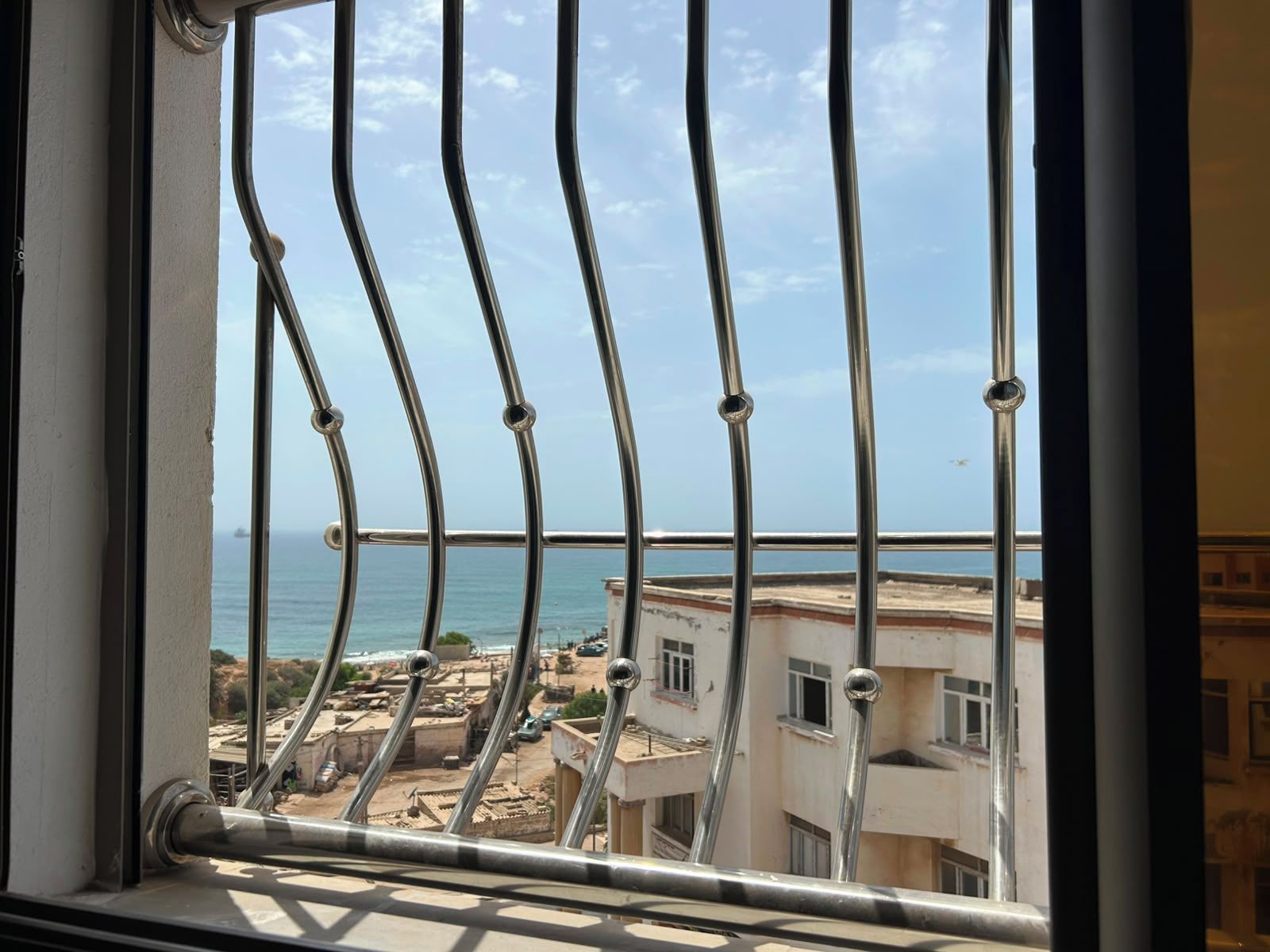 A balcony with metal railings overlooking a coastal area with buildings and a view of the sea.