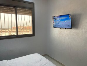 A room with a bed, a window with blinds, and a mounted TV displaying a map. - Ocean View Agadir (Agadir)
