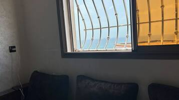 A room with a window overlooking a body of water, a power outlet, and two dark-colored cushions on a low table.