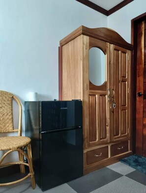 Una habitación con un armario de madera, un refrigerador negro, una silla de mimbre y una alfombra azul.