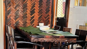 A dining area with a herringbone wood panel wall, a table set with a green tablecloth, and wooden chairs. - Noah Bed&Breakfast 3 privateStandard Room Shared Bathroom•14 mins to PPS Airport (Puerto Princesa City)
