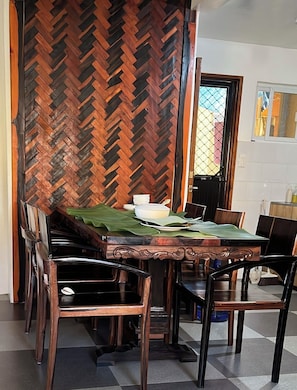 Un comedor con pared de madera en patrón de espiga, una mesa cubierta con mantel verde y sillas de madera.