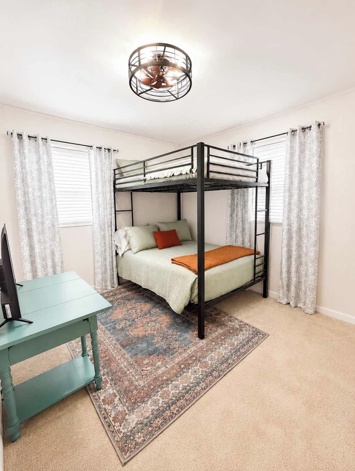 A bunk bed room with a desk and a patterned rug.