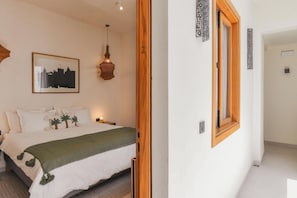A hotel room with a bed, a framed cityscape picture, a hanging light fixture, and a wooden-framed window. - Asilah (Marrakech)