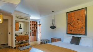 Ett hotellrum med en stor säng, ett badrum med handfat och spegel, en bokhylla och ett stort konstverk på väggen.