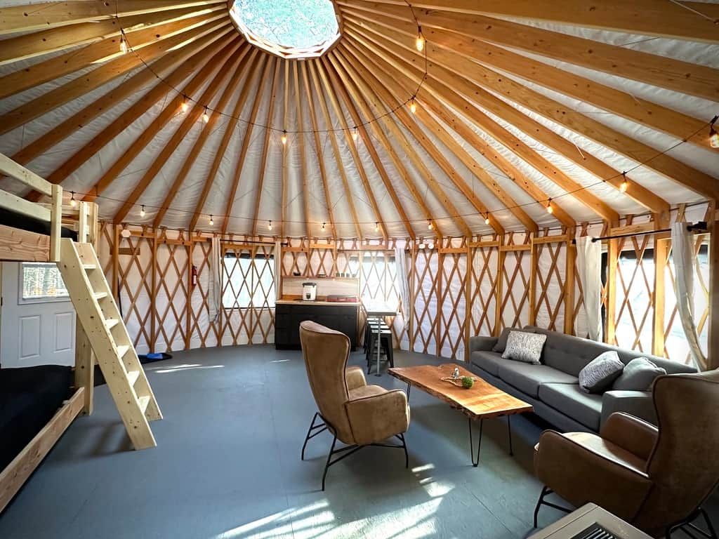 A yurt interior with a central seating area, a kitchen, and a ladder leading to an upper level.