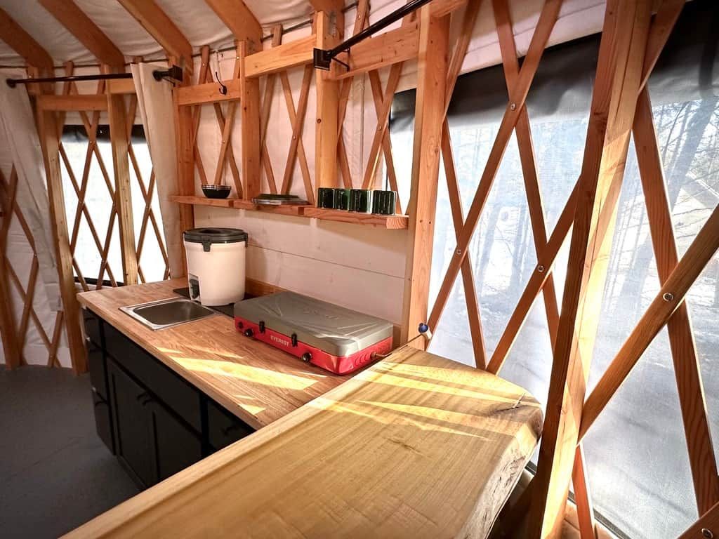 Una cucina compatta con un piano di lavoro in legno, un lavello e una valigia rossa.